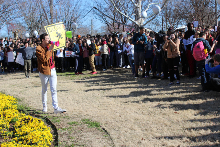 Senior Ollie Burrow leads chants to the crowd during the Walkout. His sign is a play on school zone signs, with a student crossing and bullet holes around it. (Photo by Annie Simon)