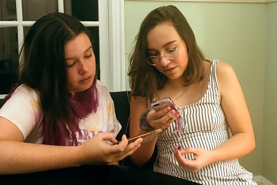 Sophomores Anna Spollen and Mary Ruth Taylor look at their phones as Mary Ruth plays a song off of YouTube. They sing a song by Twenty One Pilots together as they talk to each other about their past. (Photo by Jakob Mueller)