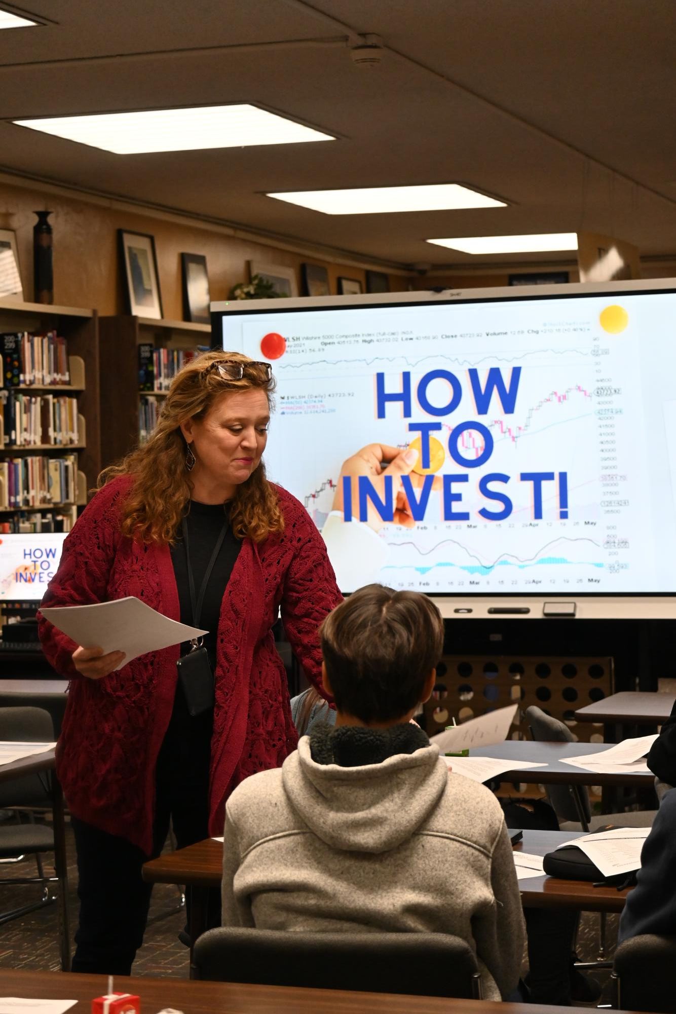 Librarian Lori Curtis passes out informational material to students who are interested in playing The Stock Market Game during third lunch Jan. 21. “I did some work this summer writing elementary curriculum for financial education, and it kind of renewed my interest,” said Curtis.